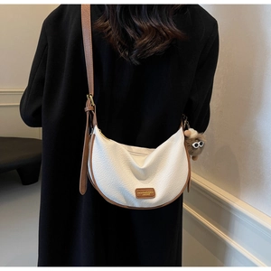 Close-up of contrast-stitch crescent bag with pebble leather and brown plush charm