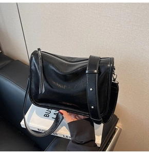 Détail de la texture en cuir ciré noir brillant et logo sur le sac à bandoulière élégant