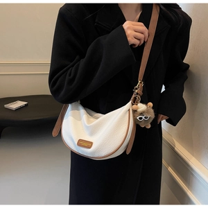 Close-up of white lychee leather crescent bag with brown trim and plush monster charm