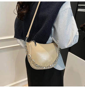 Detail of cream crescent shoulder bag with metallic moon pendants on silver chain