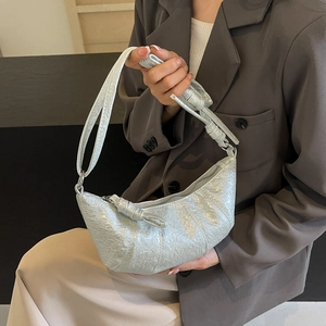 Detail of silver metallic croissant bag with pleated texture worn over a grey blazer