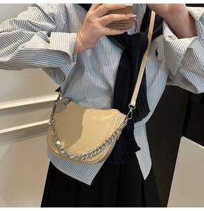 Detail of beige faux leather saddle bag with silver chain accent and slim shoulder strap