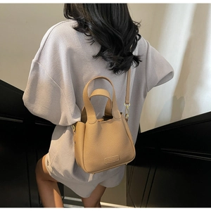 Detail of minimalist bucket bag in lychee leather showing dual handles and gold hardware