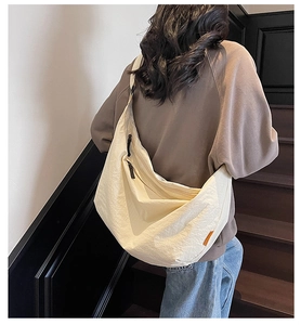 Model wearing a large off-white crescent tote bag made of textured fabric on black stairs