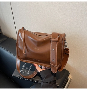 Détail d'un sac bandoulière en cuir marron foncé avec sangle cloutée et logo de marque