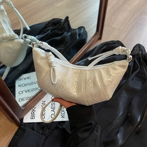 Close-up of pearl white pleated croissant bag with knotted handle and glossy texture