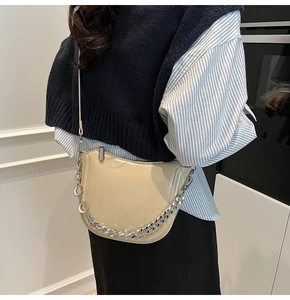 Detail of high-gloss cream saddle bag featuring chunky silver chain and slim strap