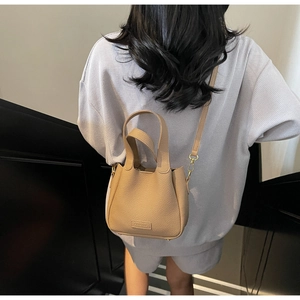 Rear view of a model carrying a khaki lychee leather bucket bag with top handle and strap