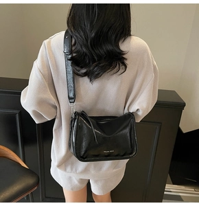 Détail du sac bandoulière noir verni brillant avec logo argenté et zip latéral