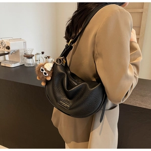 Detail view of black pebble leather moon bag with gold zipper and plush monkey charm