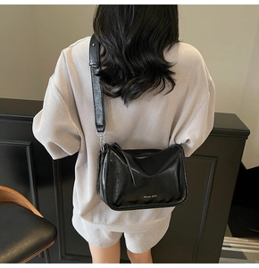Vue mannequin d'un sac bandoulière noir brillant en similicuir avec sangle large