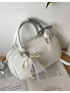 White Boston handbag in matte PU leather with pearl charm and ribbon detail on wood surface