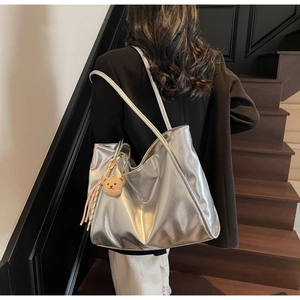 Nahaufnahme einer silbernen Metallic-Einkaufstasche mit braunem Plüschbär-Anhänger