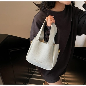 Detail showing litchi grain texture and brand leather patch on a blue bucket bag
