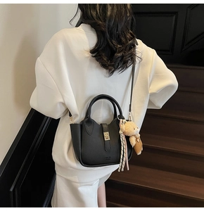 Dettaglio borsa in pelle nera con chiusura dorata, ciondolo orsetto e foulard a righe