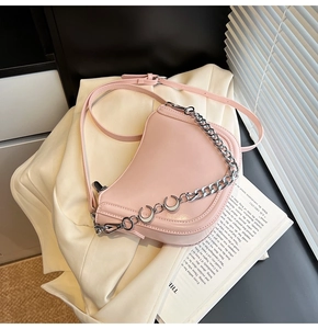 Detail of light pink saddle bag with glossy finish and silver chain accessory