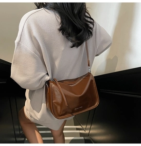 Sac bandoulière en cuir brillant marron foncé présenté dans un escalier pour le quotidien