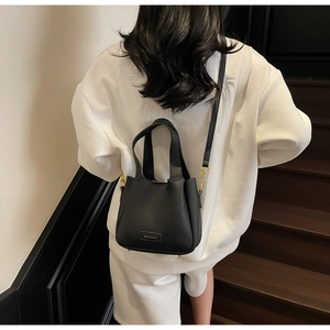 Detail of black pebbled leather bucket bag with gold hardware worn by a model