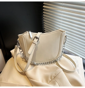 Detail view of beige crescent saddle bag with silver chain and C-shaped metal charm