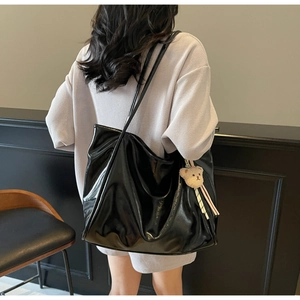 Nahaufnahme der glänzenden schwarzen Lackleder-Einkaufstasche mit braunsgtasche mit Plüschbären-Anhänger