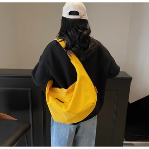 Detail of bright yellow waterproof nylon crescent bag with orange brand tag shown on model