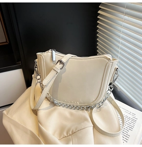 Chic cream leather saddle bag with silver chain detail on soft fabric background