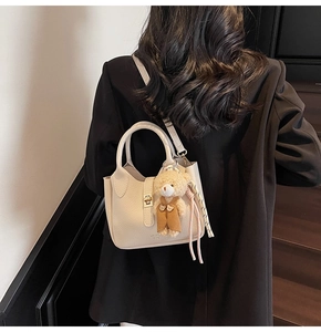 Borsa beige a grana di litchi con ciondolo a orsetto e tracolla indossata da una modella