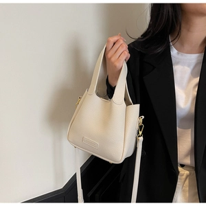 Detail of cream leather bucket bag with gold hardware and logo on model in black blazer