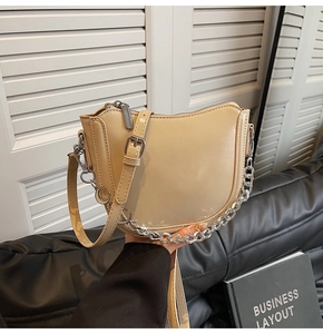 Detail of beige crescent shoulder bag with silver chunky chain and moon charm on a sofa