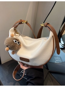Chic white half-moon crossbody bag with brown leather trim and plush charm detail