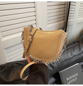 Detail of beige faux leather saddle bag with chunky metal chain and adjustable strap