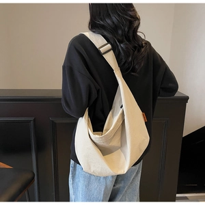Close-up of cream canvas crescent bag with wide adjustable shoulder strap on person