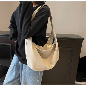 Detail of a large beige nylon hobo bag with adjustable strap worn by a model
