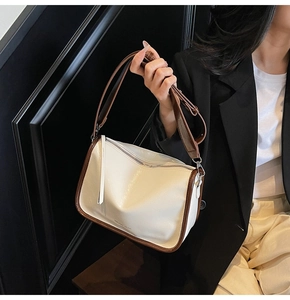 Détail du sac à main en cuir verni blanc avec bordure marron porté sur un tailleur noir