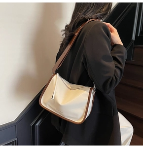 Détail du sac à bandoulière beige avec bordure marron porté par un mannequin