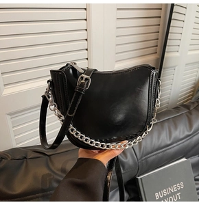 Detail of a black glossy PU saddle bag featuring silver chain decor and adjustable strap