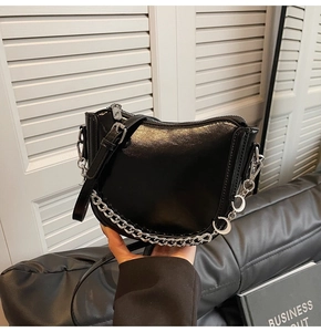 Close-up of black patent leather saddle bag with silver chain and U-shaped design
