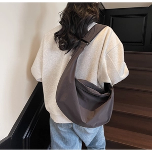 Rear view of dark brown crescent hobo bag made of matte nylon worn by a female model
