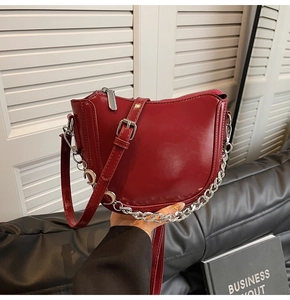 Detail of dark red crescent shoulder bag with glossy finish and silver chain crescent charm