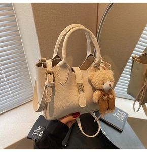 Dettaglio borsa tote in pelle crema motivo litchi con chiusura dorata e ciondolo orso