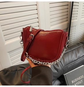 Detail of burgundy semi-circle bag featuring glossy finish and silver chain strap