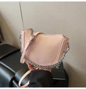 Close-up of light pink saddle bag with glossy finish and silver chain detail