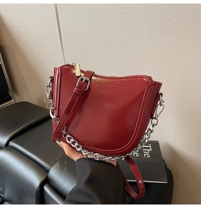 Detail of bright red patent leather handbag featuring a silver chain and curved silhouette