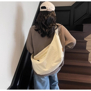 Model wearing a large cream crescent shoulder bag on a shoulder in a casual urban setting