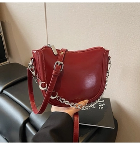 Detail of burgundy patent leather saddle bag with silver moon charm chain strap