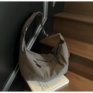 Detail of grey nylon tote bag with orange label and adjustable strap on wooden steps