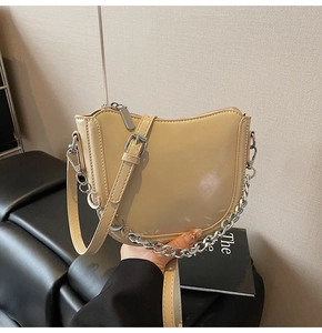 Detail of light khaki saddle bag with shiny leather finish and silver chain strap