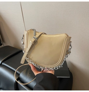 Detail of glossy beige patent leather saddle bag with silver chain and U-shaped design