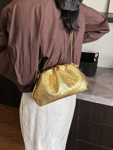 Golden pleated dumpling bag with chain strap styled on model in minimalist interior