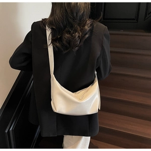 Close-up of minimalist cream white half-moon hobo bag worn with a black blazer